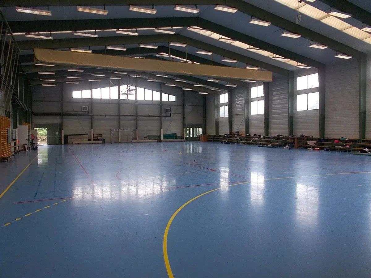 Interior of a large indoor sports hall with a blue court floor.