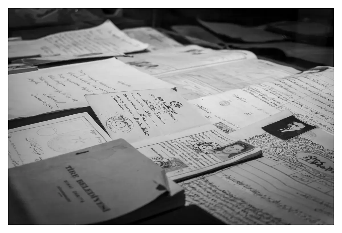 Black-and-white spread of old documents and identity papers with stamps and portrait photos.