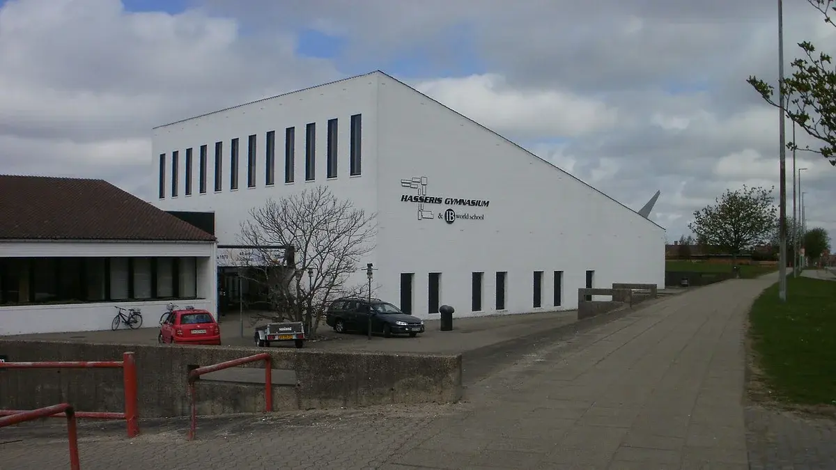 White building of Hasseris Gymnasium with parked cars and cloudy sky