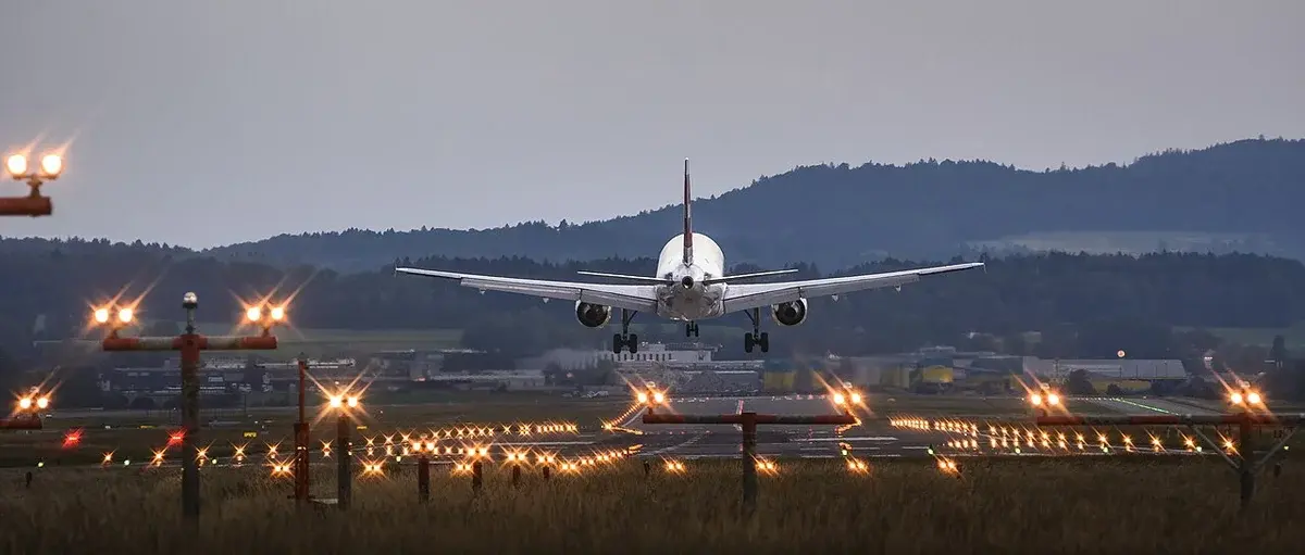 A Swiss airplane approaching landing at Zurich Airport at dusk with runway lights glowing.