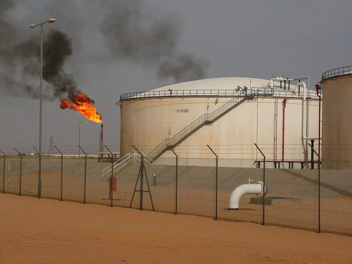 Oil tanks at a desert refinery with a gas flare burning.