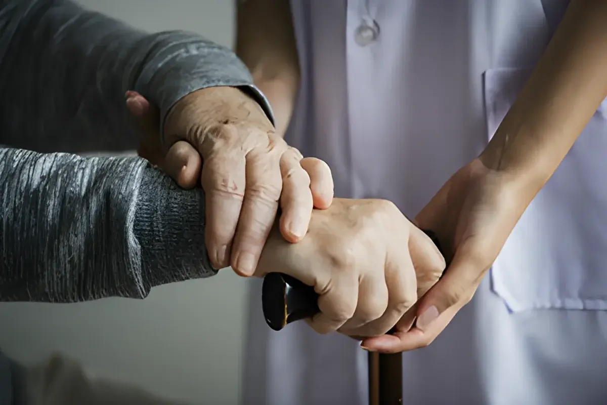 Younger person holding elderly person's hand with cane