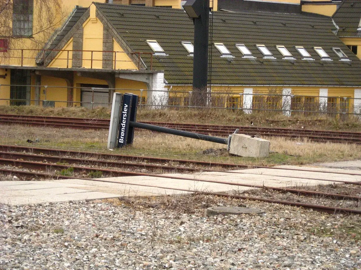 A fallen railway sign lies beside tracks near a yellow building.