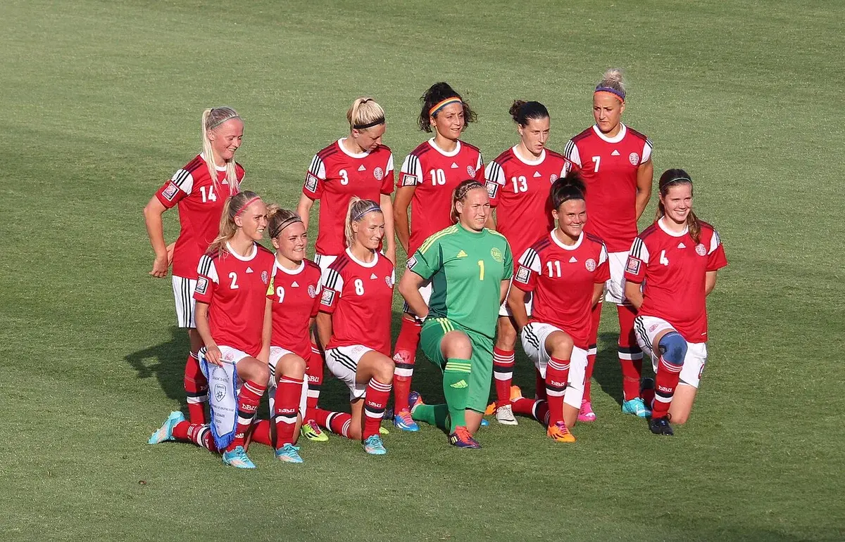 Women’s soccer team in red uniforms posing for a group photo on the field.
