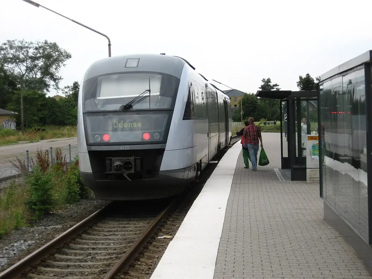 A modern train at a station platform with a few people nearby.