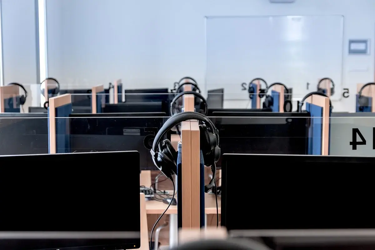 Rows of computer workstations with monitors and headsets in a classroom.