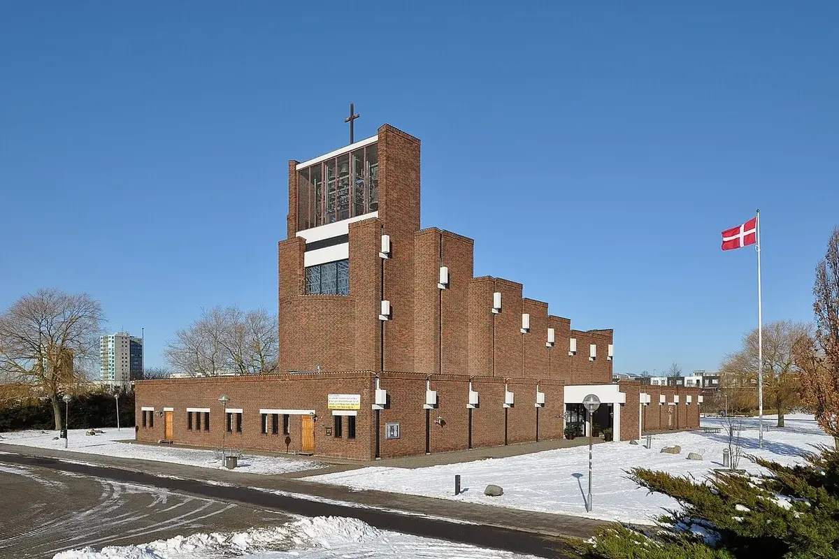 A brick church in winter with a Danish flag and a cross on the roof.