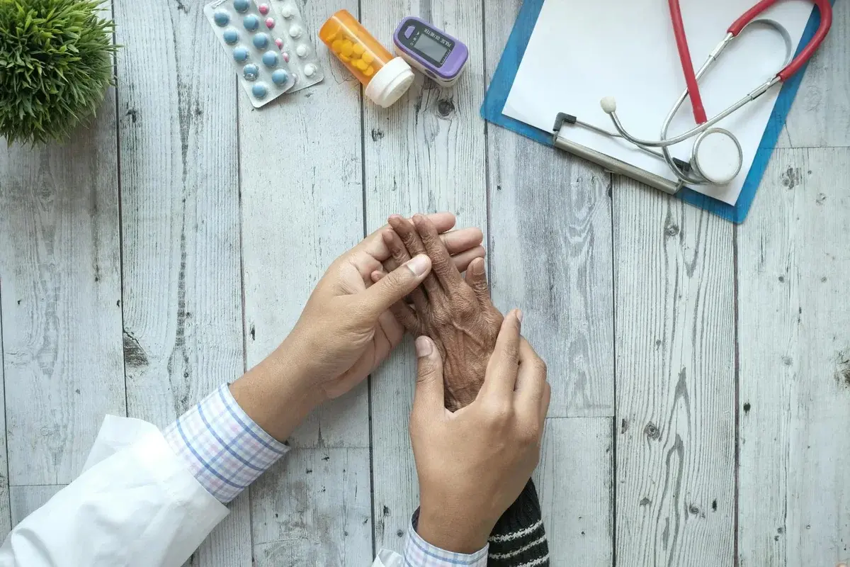 Doctor holding elderly patient's hands with medical tools nearby