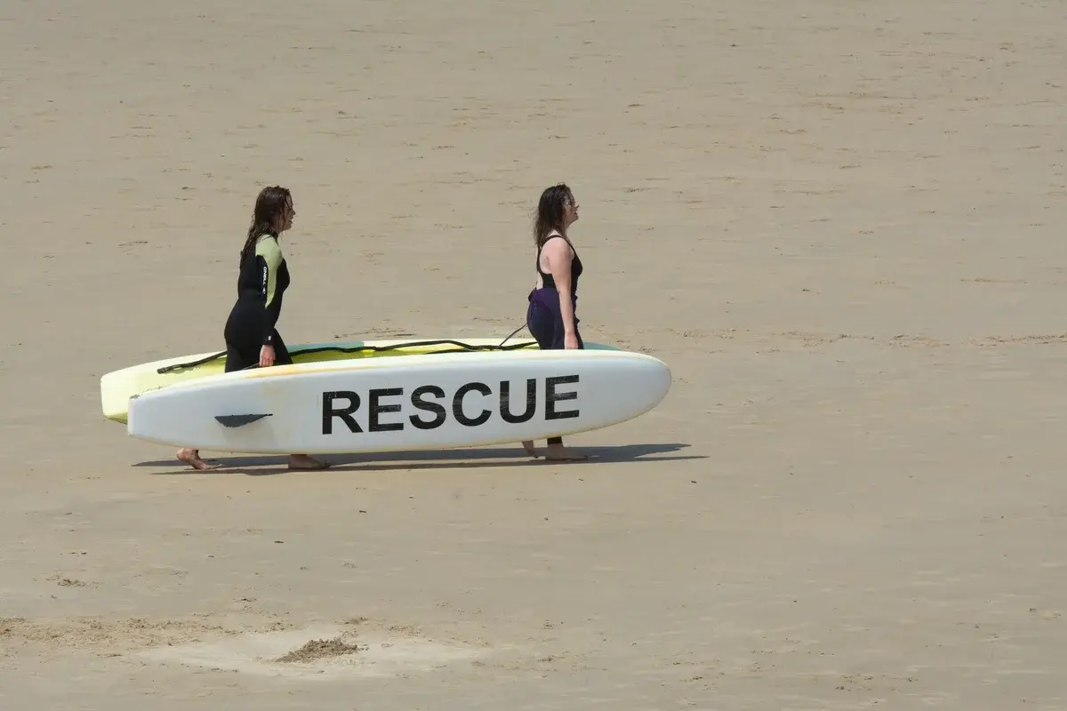 Two women carrying a rescue board on sandy beach