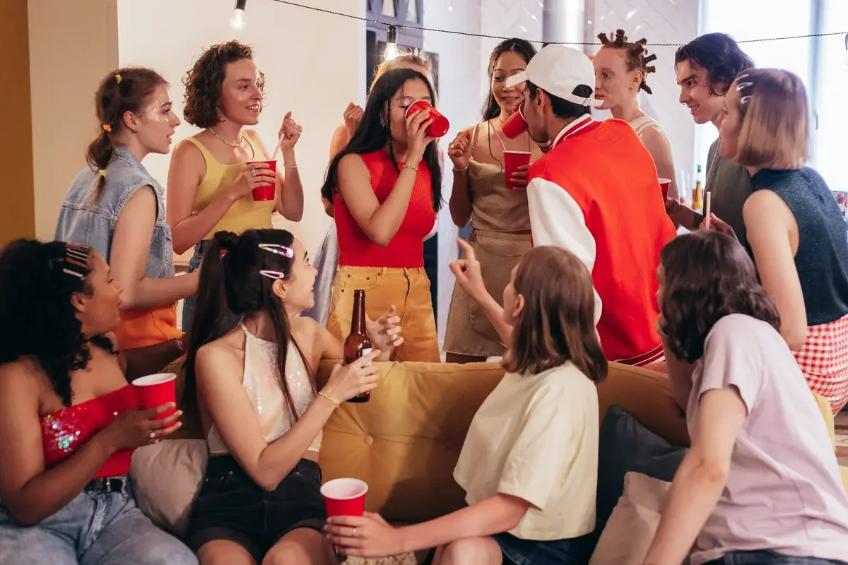 A group of young people chatting and drinking at an indoor house party.