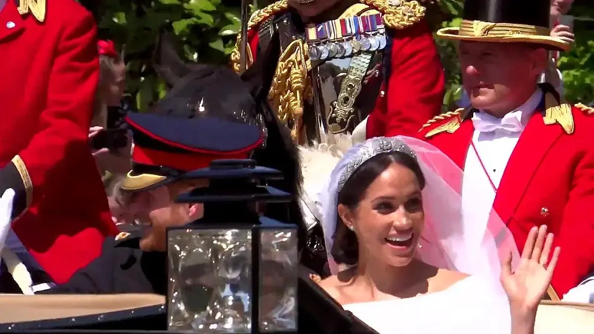 Prince Harry and Meghan smiling and waving in a horse carriage