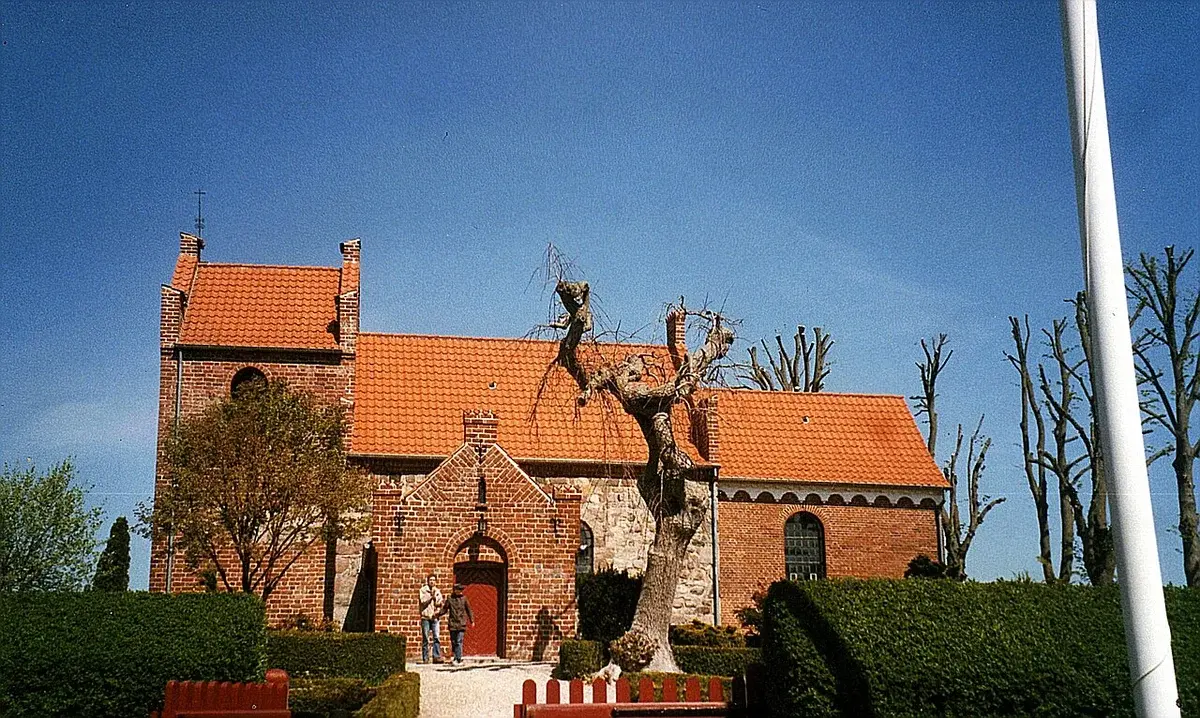 Red brick Danish village church with orange roof and two people walking in front