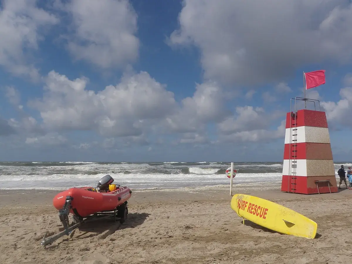 Lifeguard tower with red flag, rescue boat and surf rescue board on a sandy beach with cloudy sky