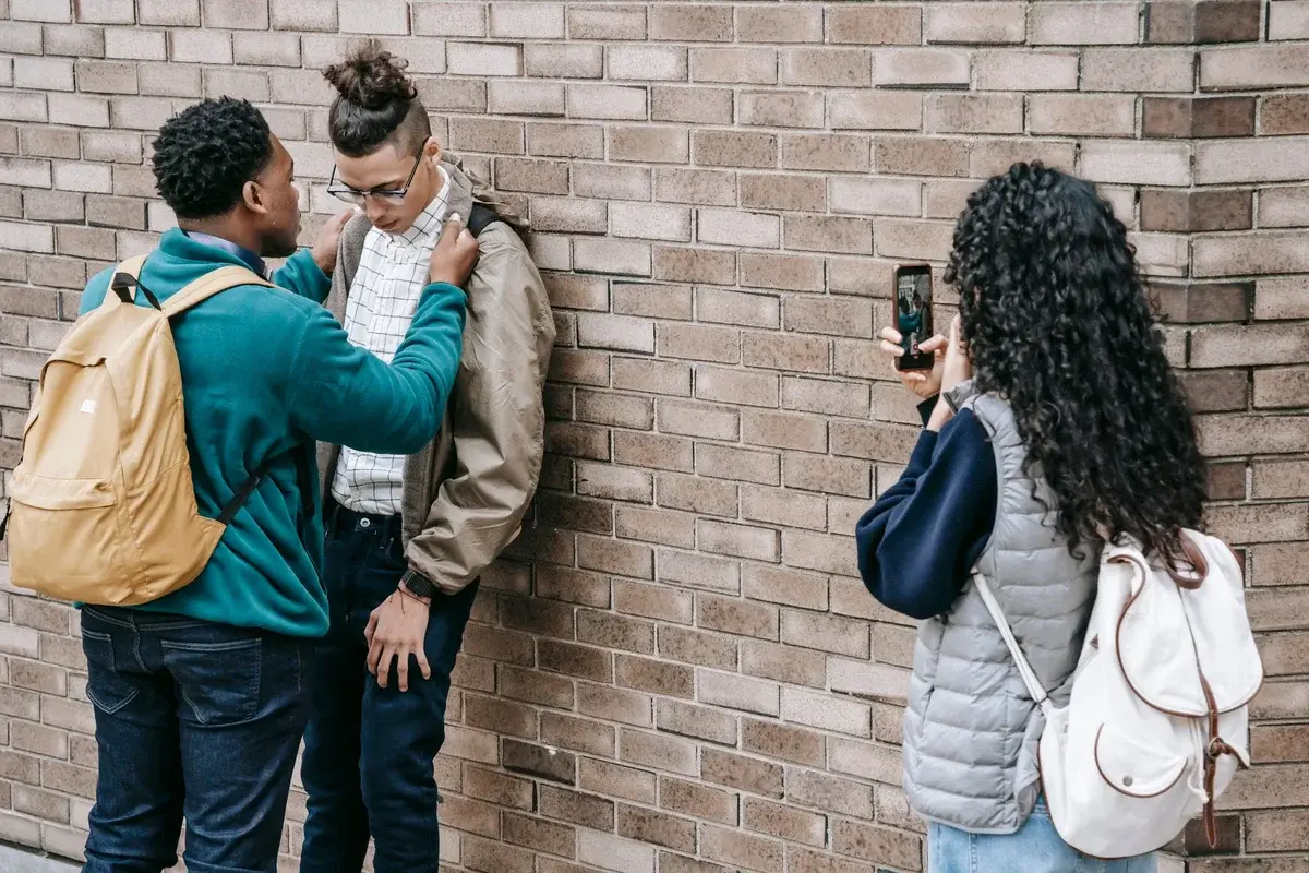 Two students confront a classmate while another films them with a smartphone.