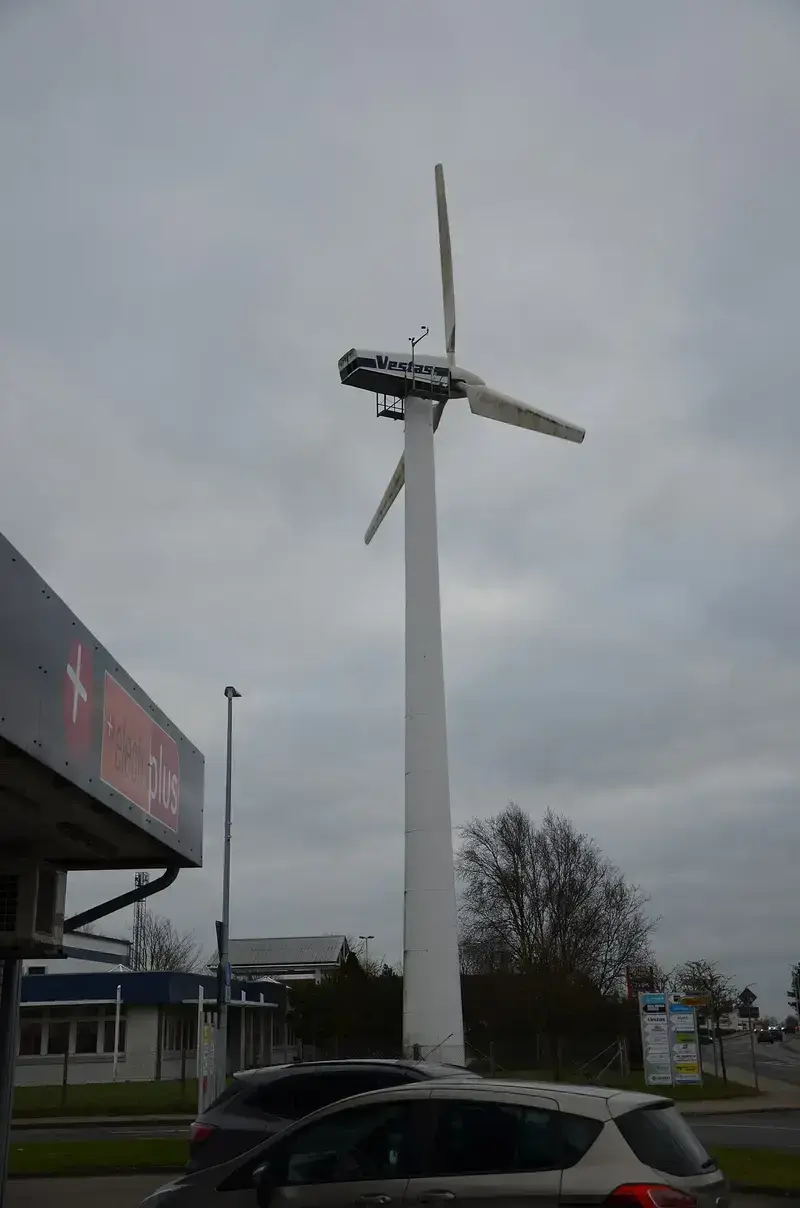 Vestas wind turbine by roadside with cars and buildings