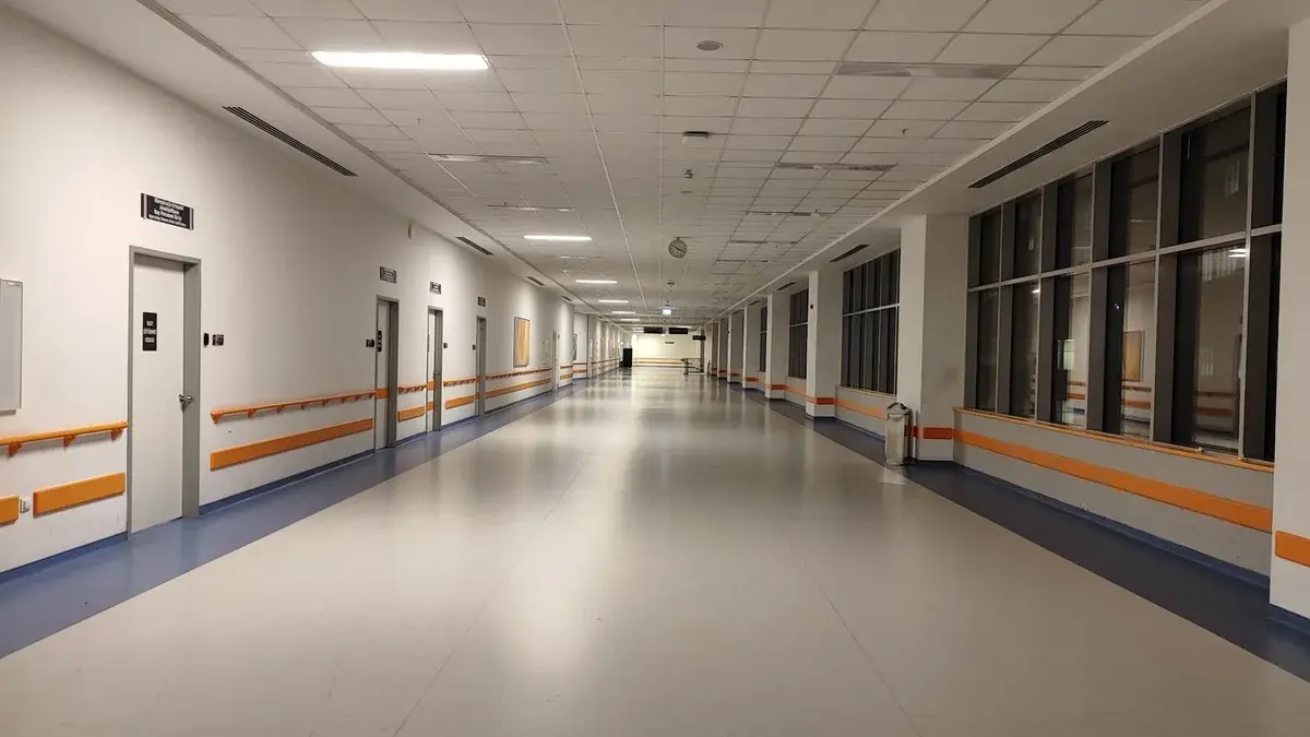 An empty modern hospital corridor with orange handrails and large windows.
