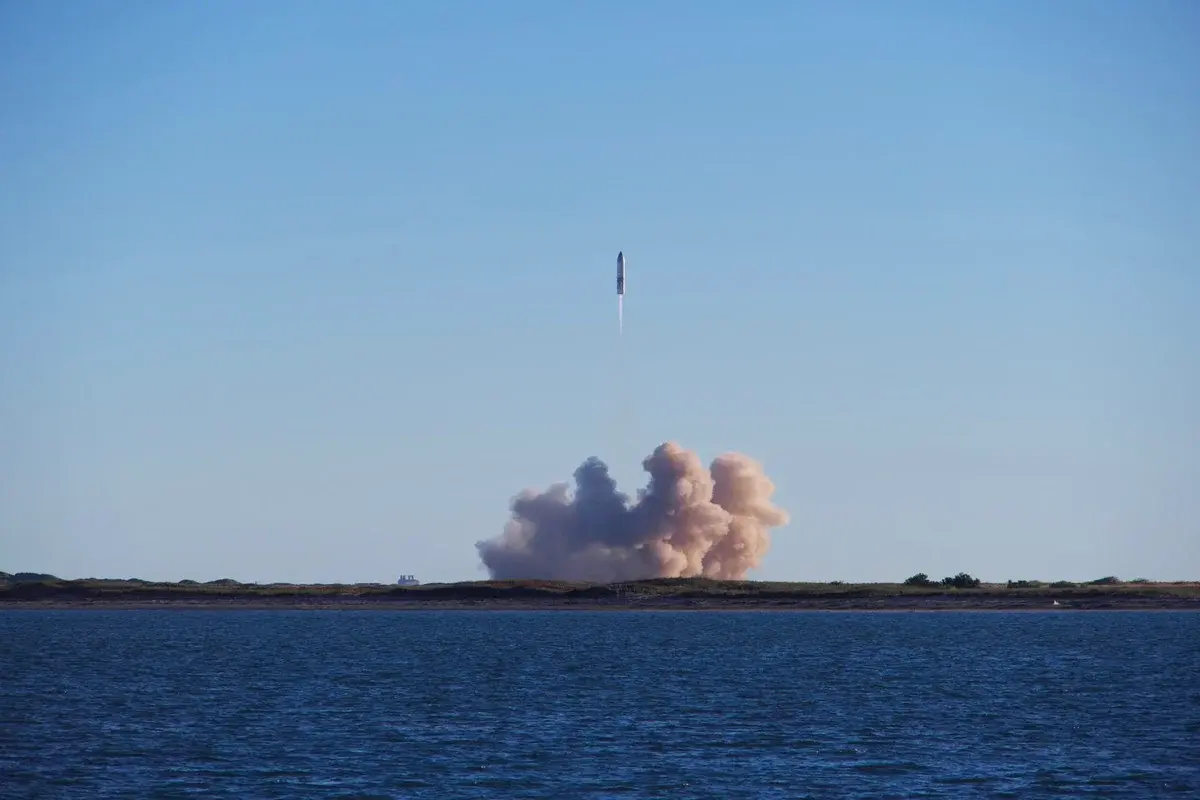 Rocket launching over coastal land with water in foreground