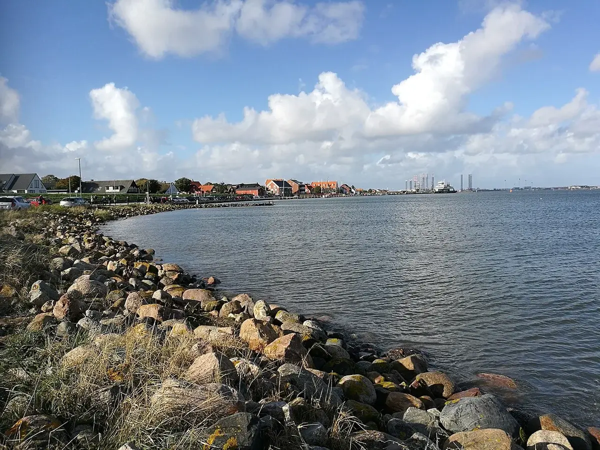 Rocky coastline with water, houses, and a cloudy sky at Nordby on Fanø.