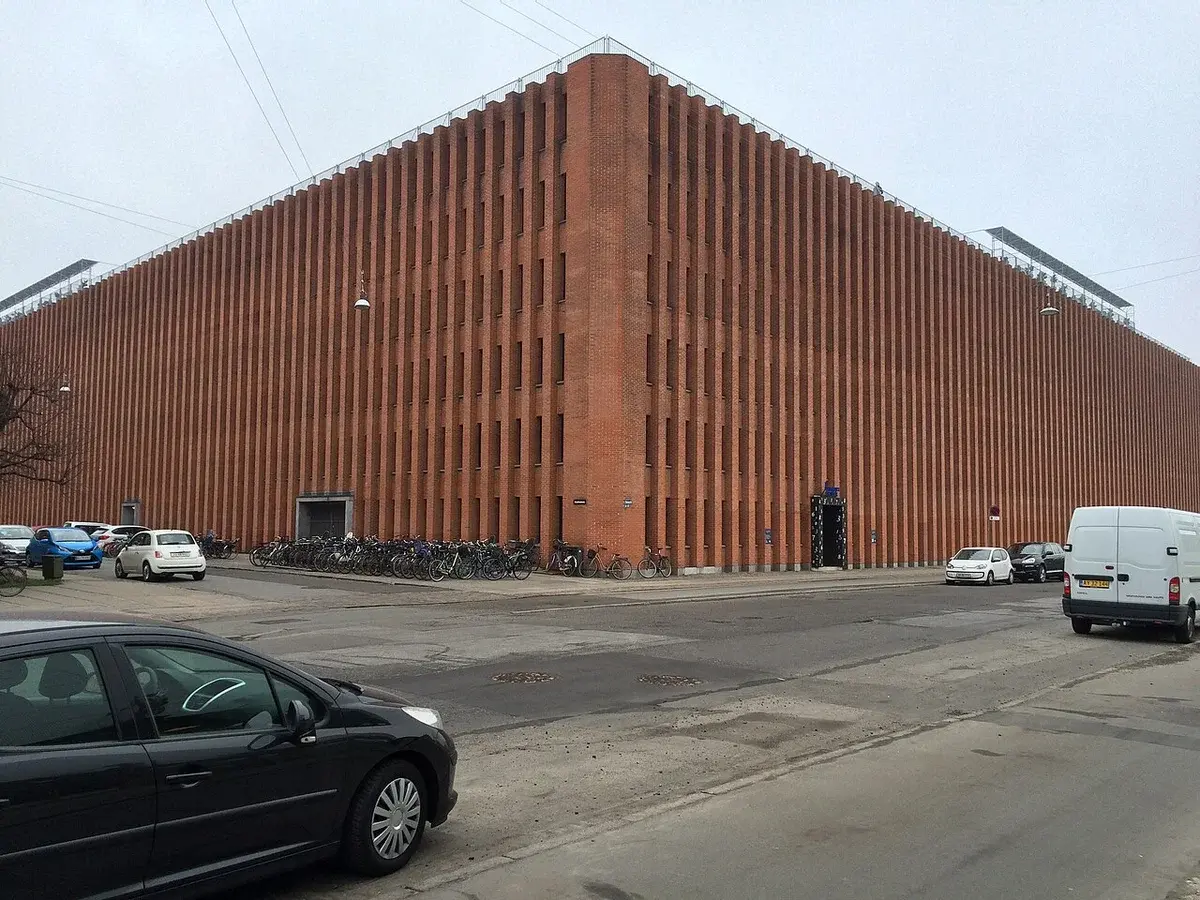 Red brick facade of Danmarks Statistik building at street corner with parked bicycles and cars