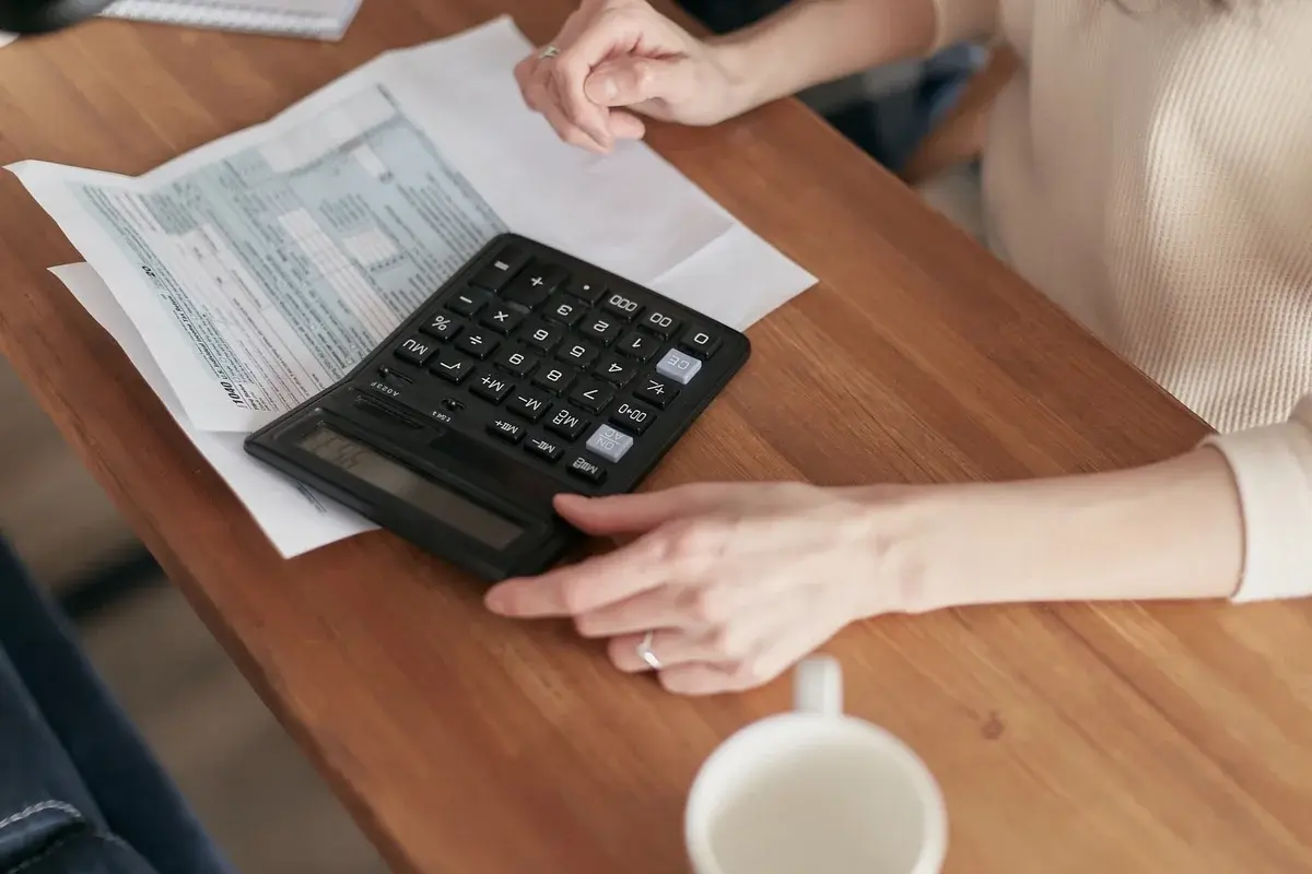 Person using a calculator with paperwork on a wooden table