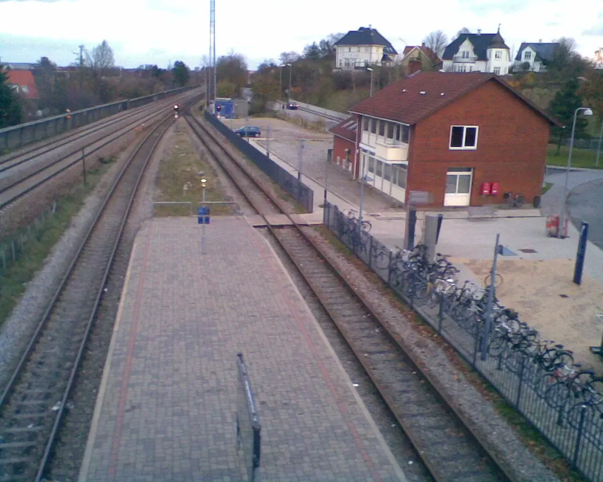 Railway tracks beside a platform and red brick station building at Viby J Station in Aarhus.