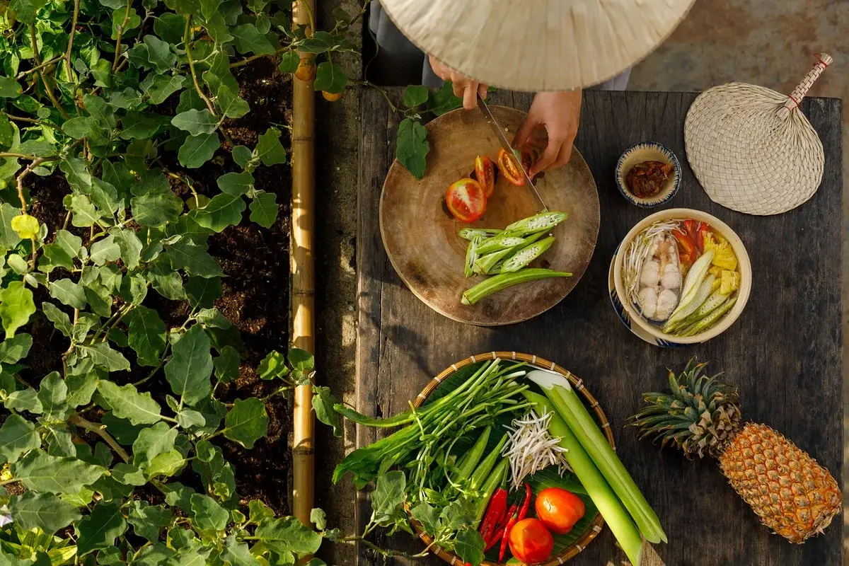 Overhead view of a woman preparing Vietnamese ingredients on a wooden table outdoors.