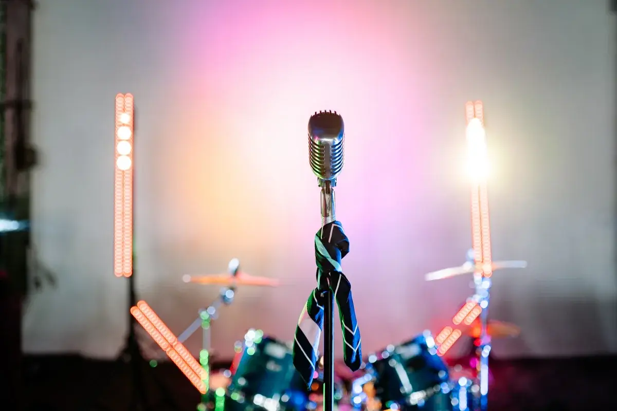 A retro microphone on a stage with colorful lights and a drum kit in the background.