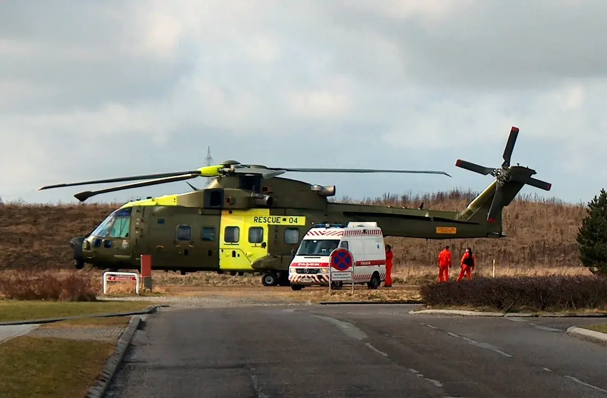 A rescue helicopter and ambulance parked on a road with three orange-suited workers nearby.