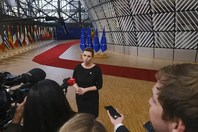 Mette Frederiksen speaking to journalists with EU flags and red carpet in background