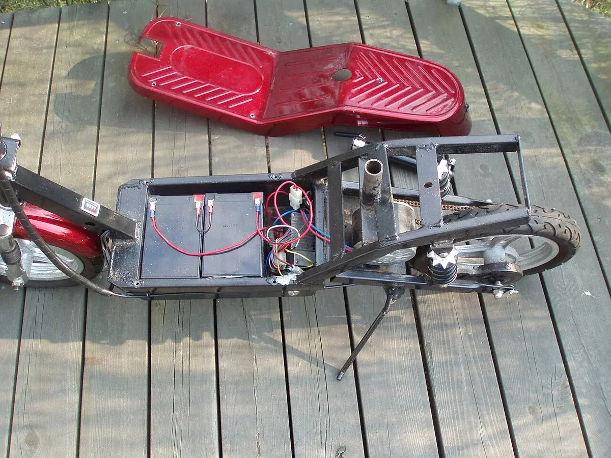 A partially disassembled red electric scooter on a wooden deck.