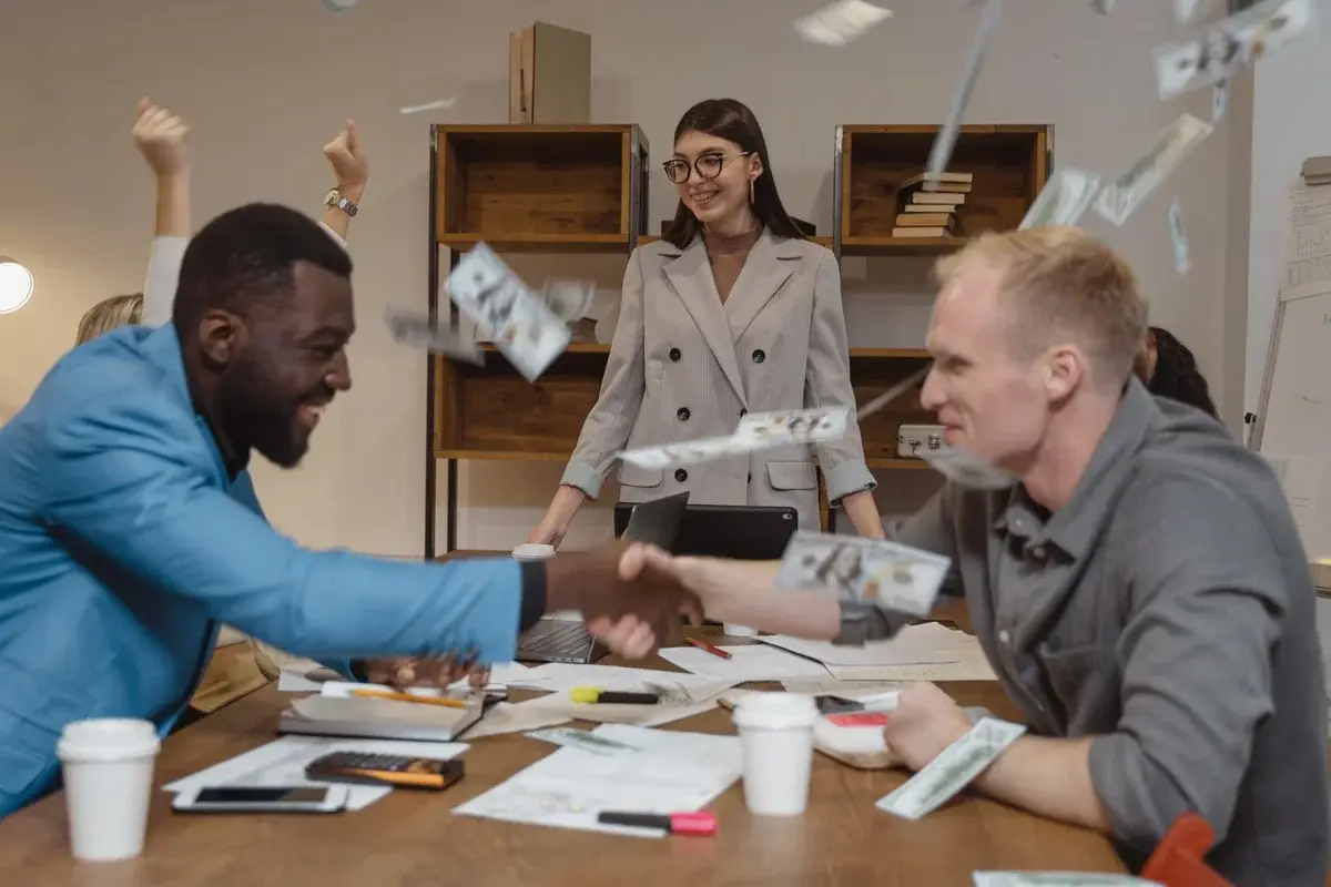 Business colleagues shaking hands with money flying around in celebration