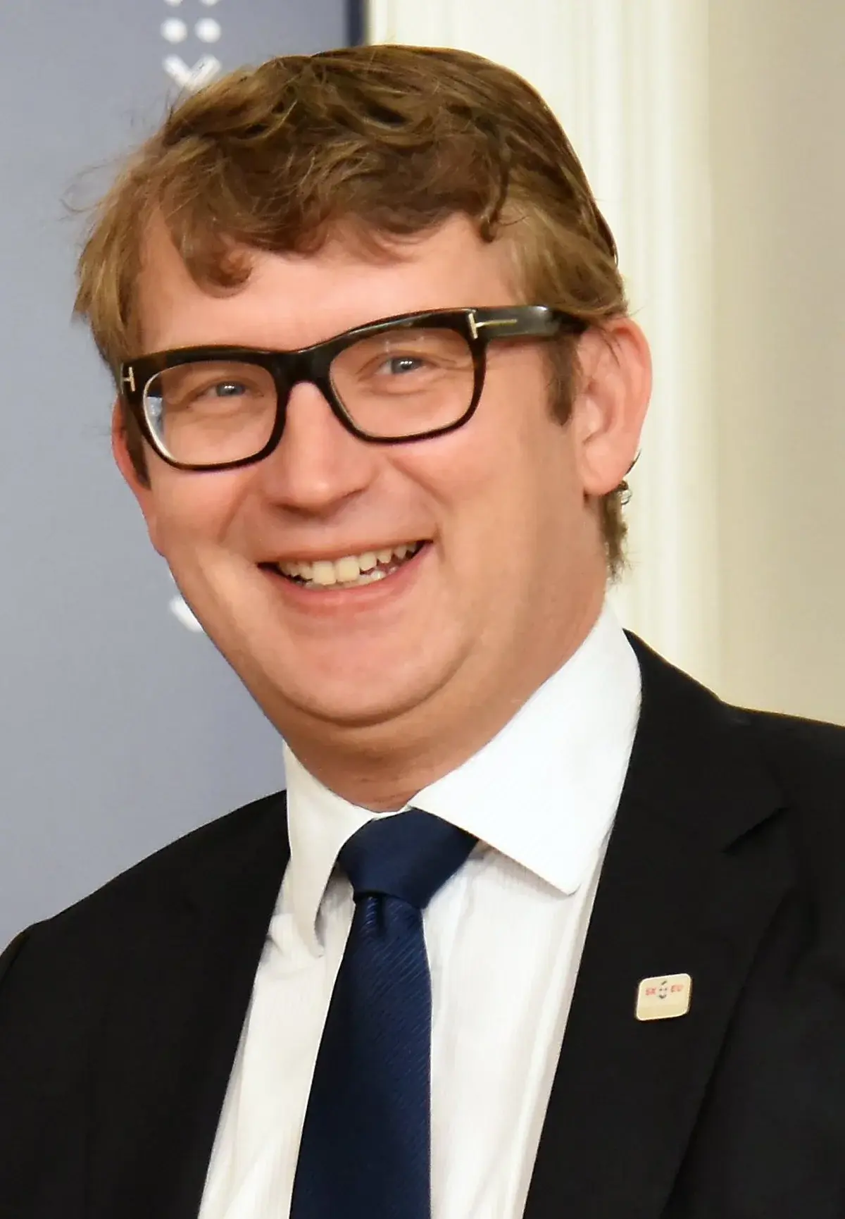 Portrait of Troels Lund Poulsen smiling in a suit and glasses.
