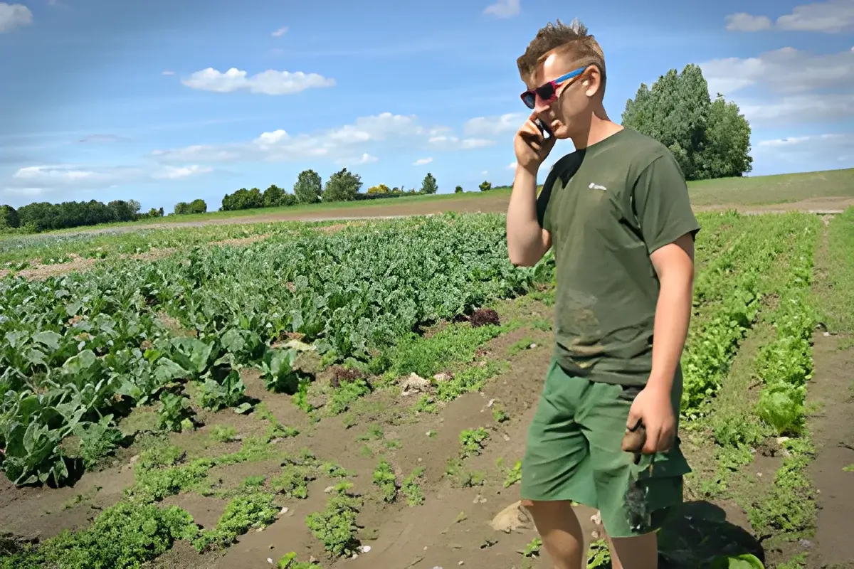 A man talks on a mobile phone while standing in a vegetable field.