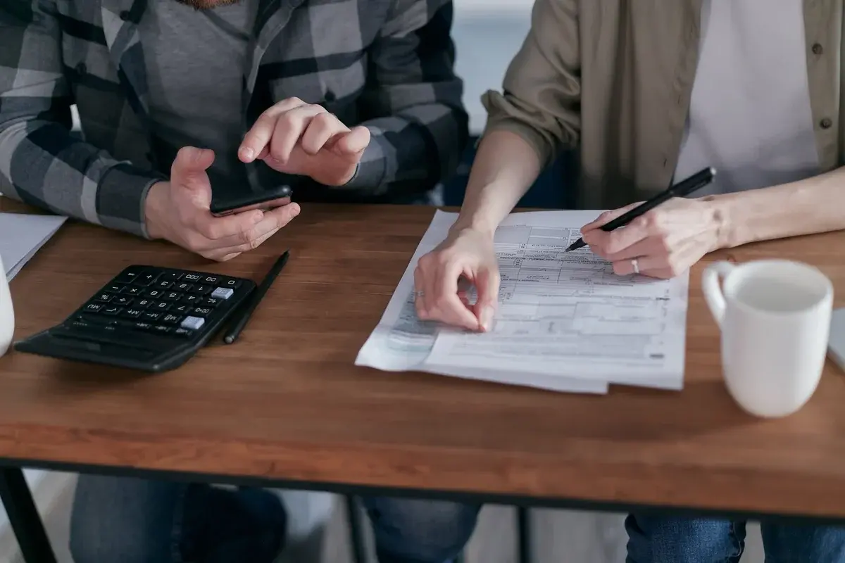 Two people review tax documents at a table with a calculator and pens.