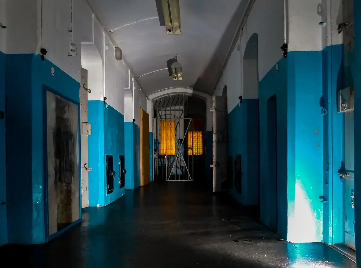 A dim prison corridor with barred gates and blue-and-white walls.