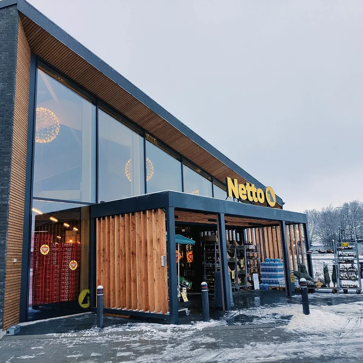 Front of Netto supermarket with wooden facade and glass windows on snowy day