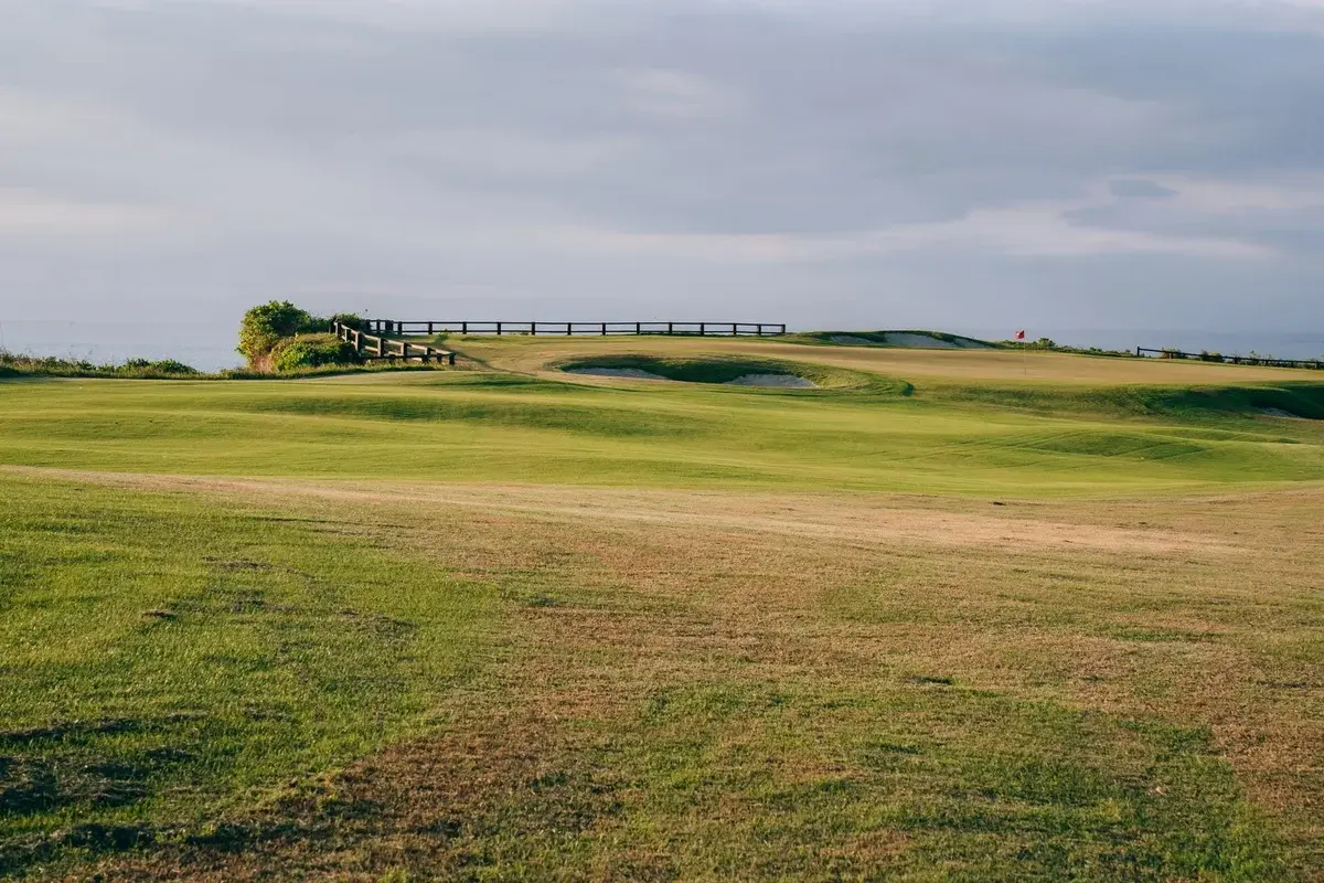 Wide view of a green golf course under cloudy skies