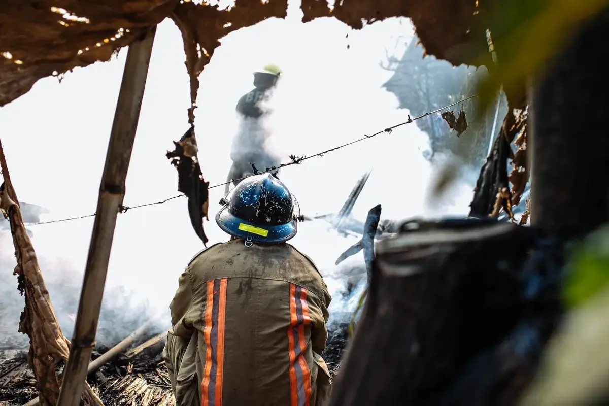 Firefighter sitting amid smoky debris while another stands in the background
