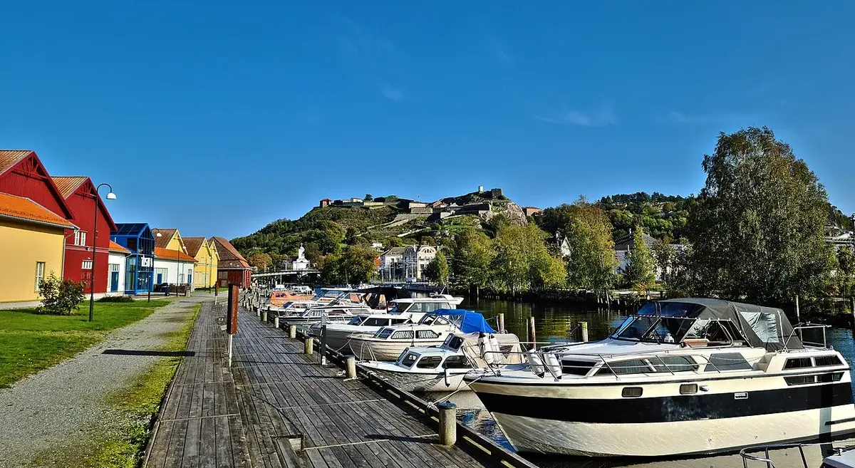 Boats docked along a waterfront in Halden with Fredriksten Fortress on a hill in the background.