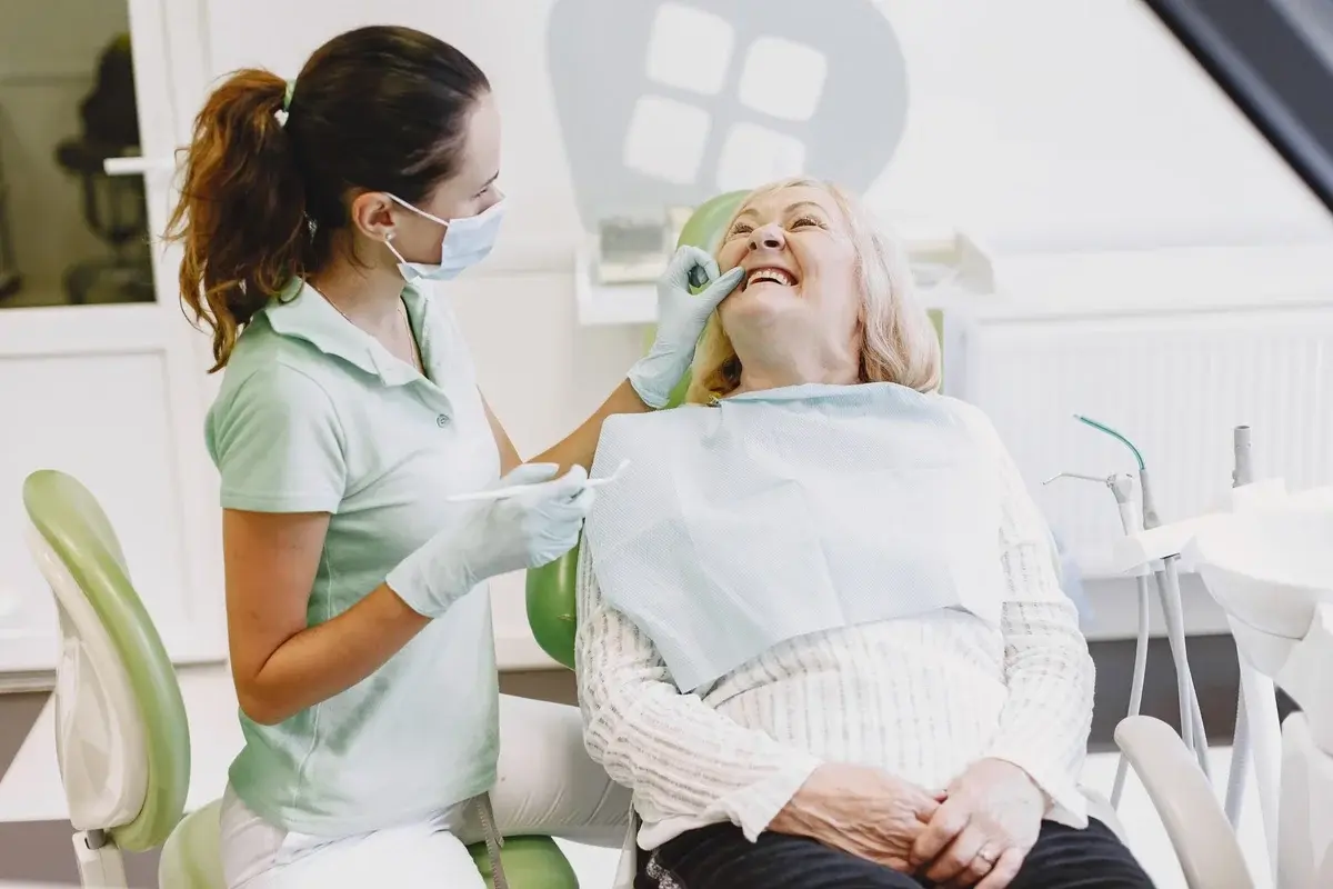 A female dentist examines an elderly woman in a dental chair.