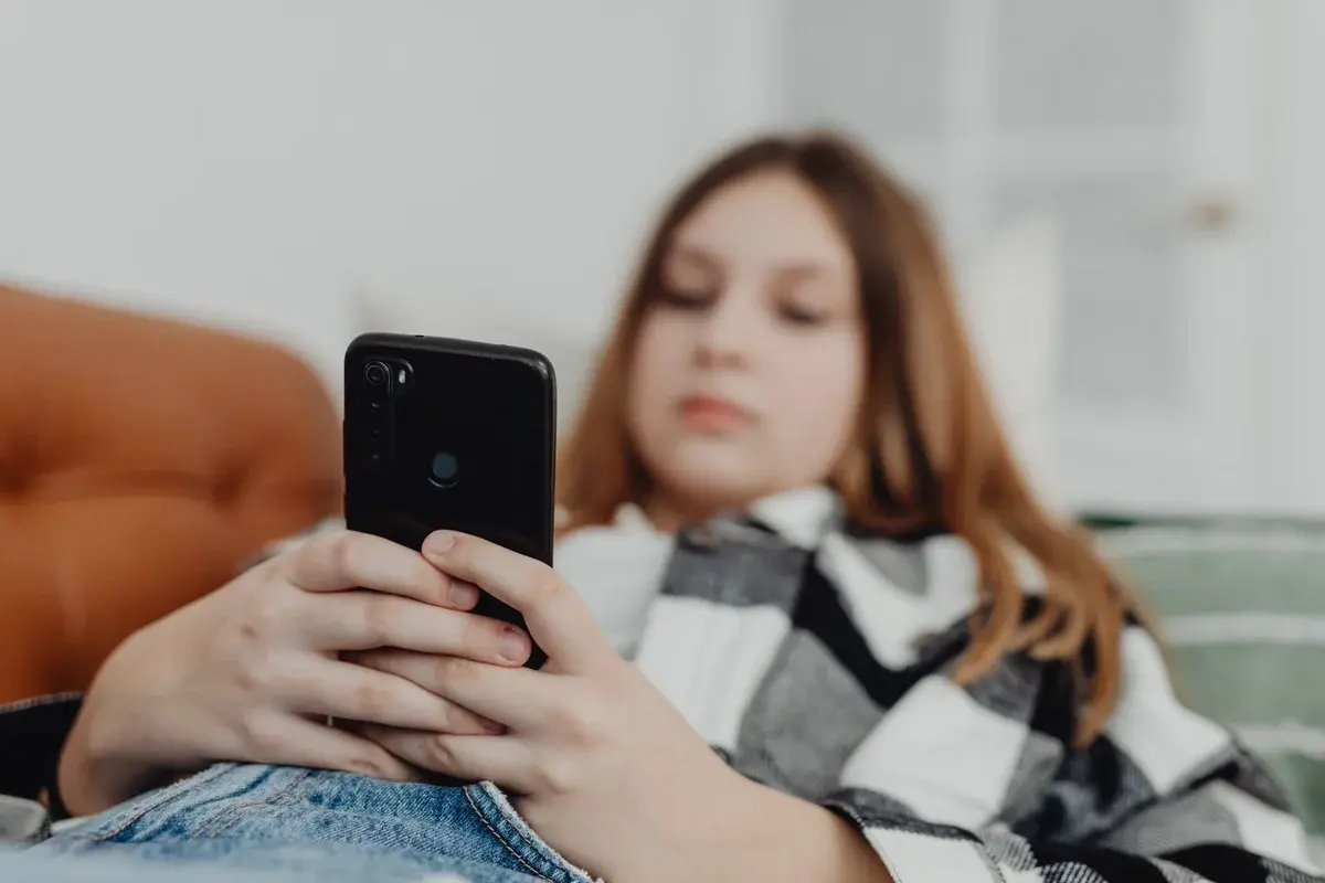Teenage girl relaxing on a sofa while using a smartphone.
