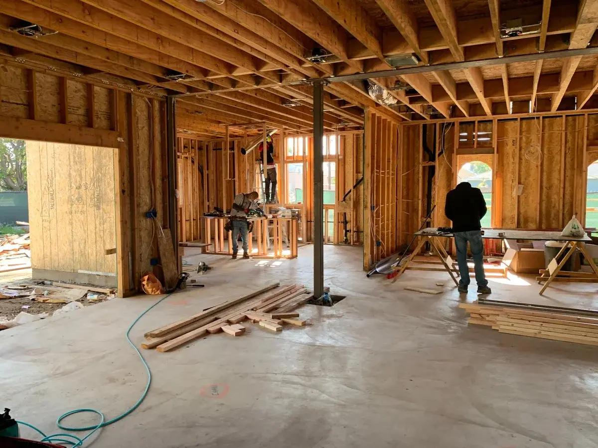 Construction workers inside a house under construction with exposed wooden framing.