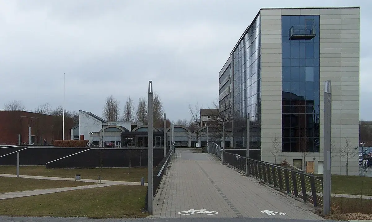 Modern town hall building with a glass facade and a pedestrian and bicycle path leading to the entrance under a cloudy sky.