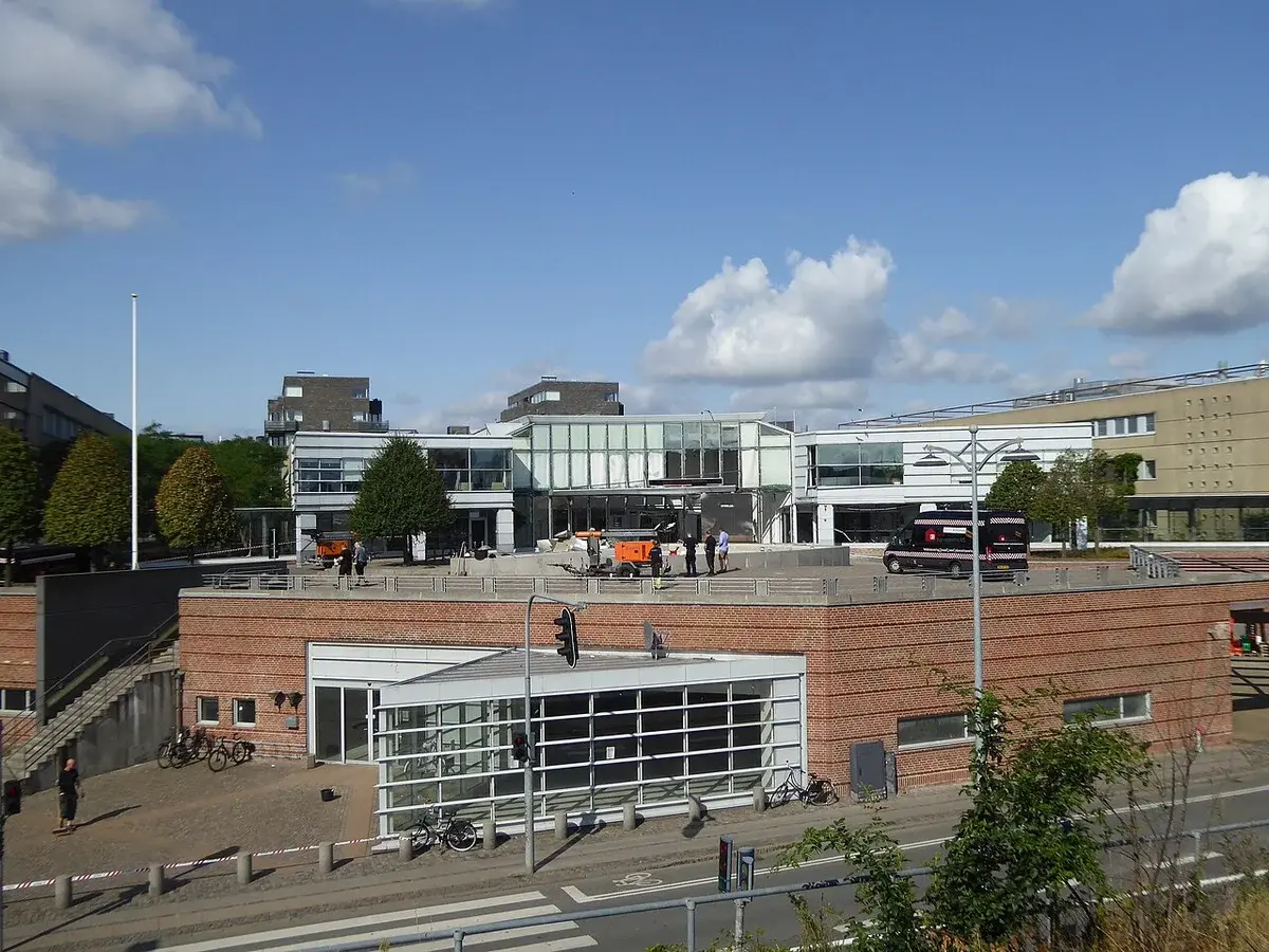 Exterior view of the Danish Tax Agency building in Copenhagen on a clear day, with people on the rooftop and bicycles nearby.