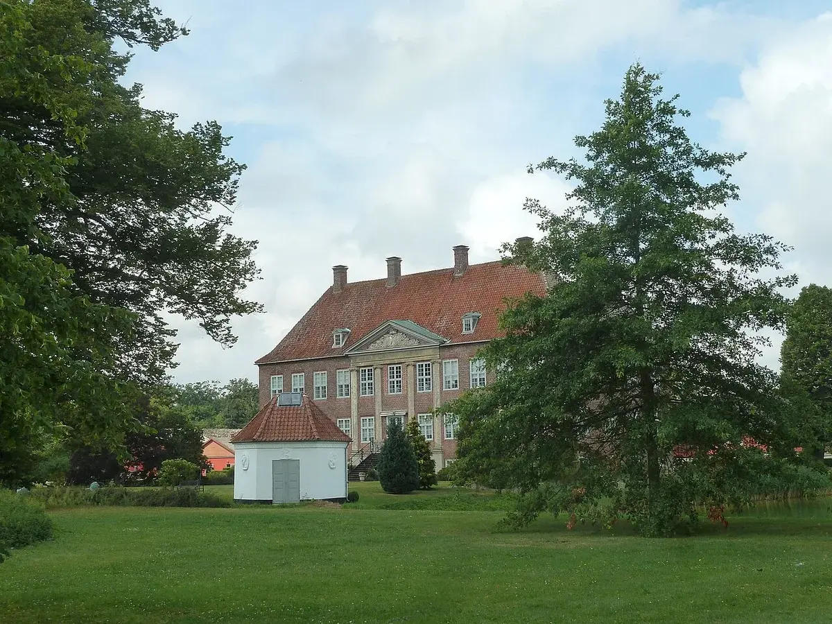 Front view of a historic Danish manor house surrounded by trees and lawn.