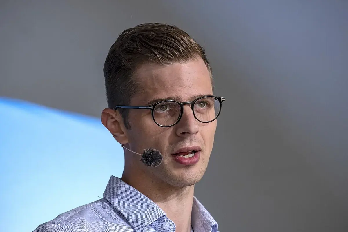 A man wearing glasses and a headset microphone speaks on stage.
