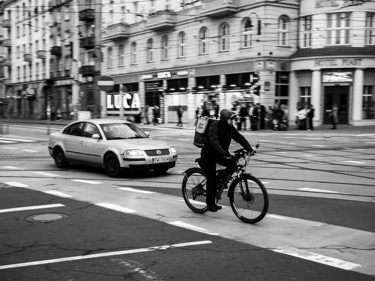Black-and-white image of a cyclist riding on a city street with a car nearby.