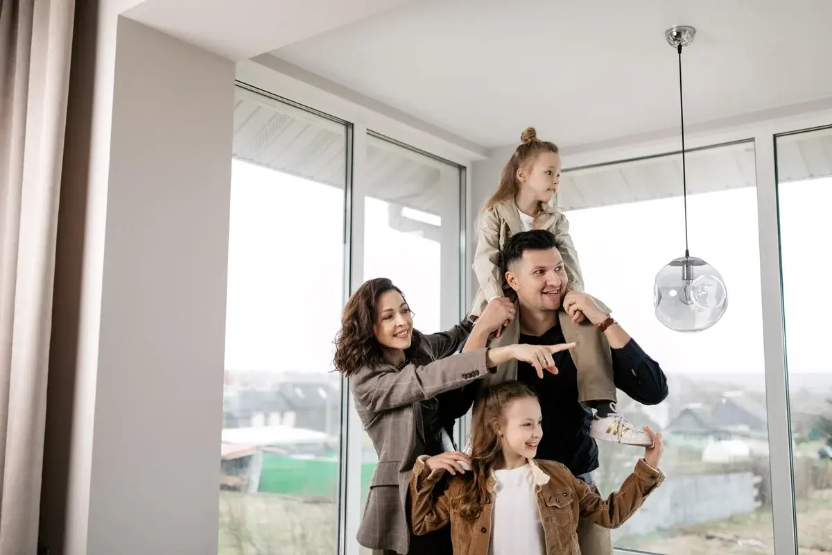 A family of four in a bright modern home, with a child on the father's shoulders.