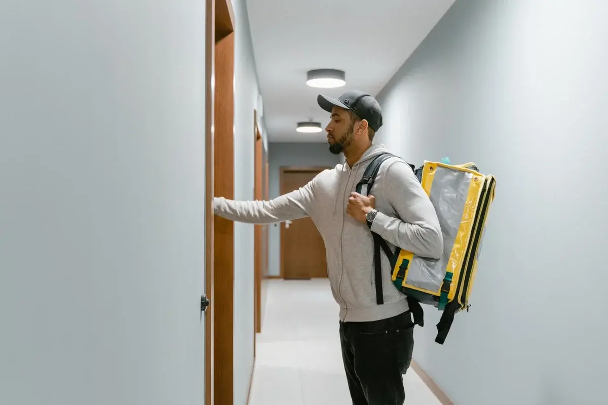 Courier knocking on apartment door with food delivery backpack