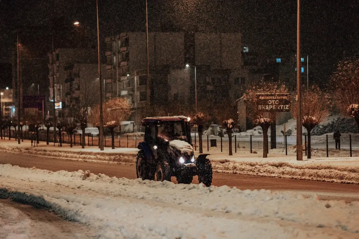 Tractor plowing snow on city street at night